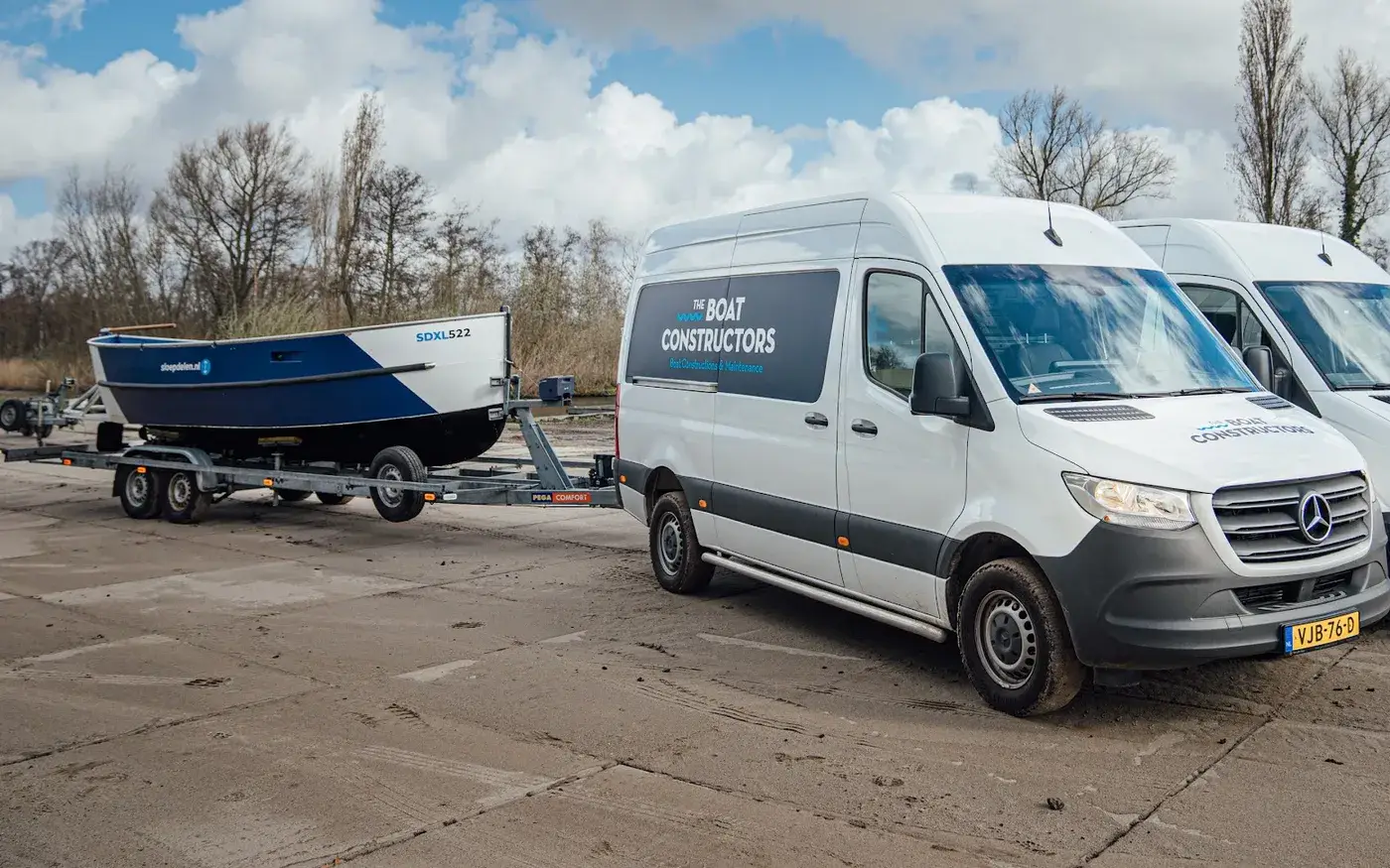 A boat on a trailer beside a white service van, ready to move to another dock