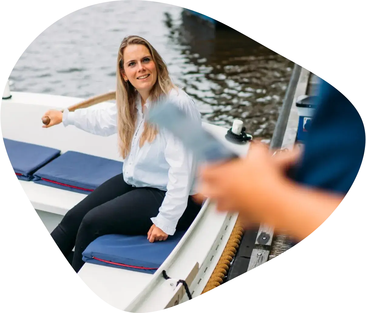 A woman with her hand on the tiller of a moored open boat, smiling at someone on the dock