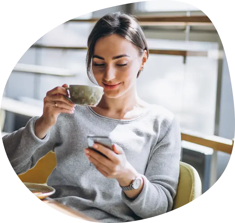 A woman holding a cup of coffee, checking her phone indoors