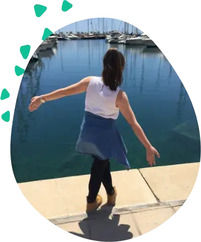 A woman stands with her arms spread on a stone quay, looking out over a marina
