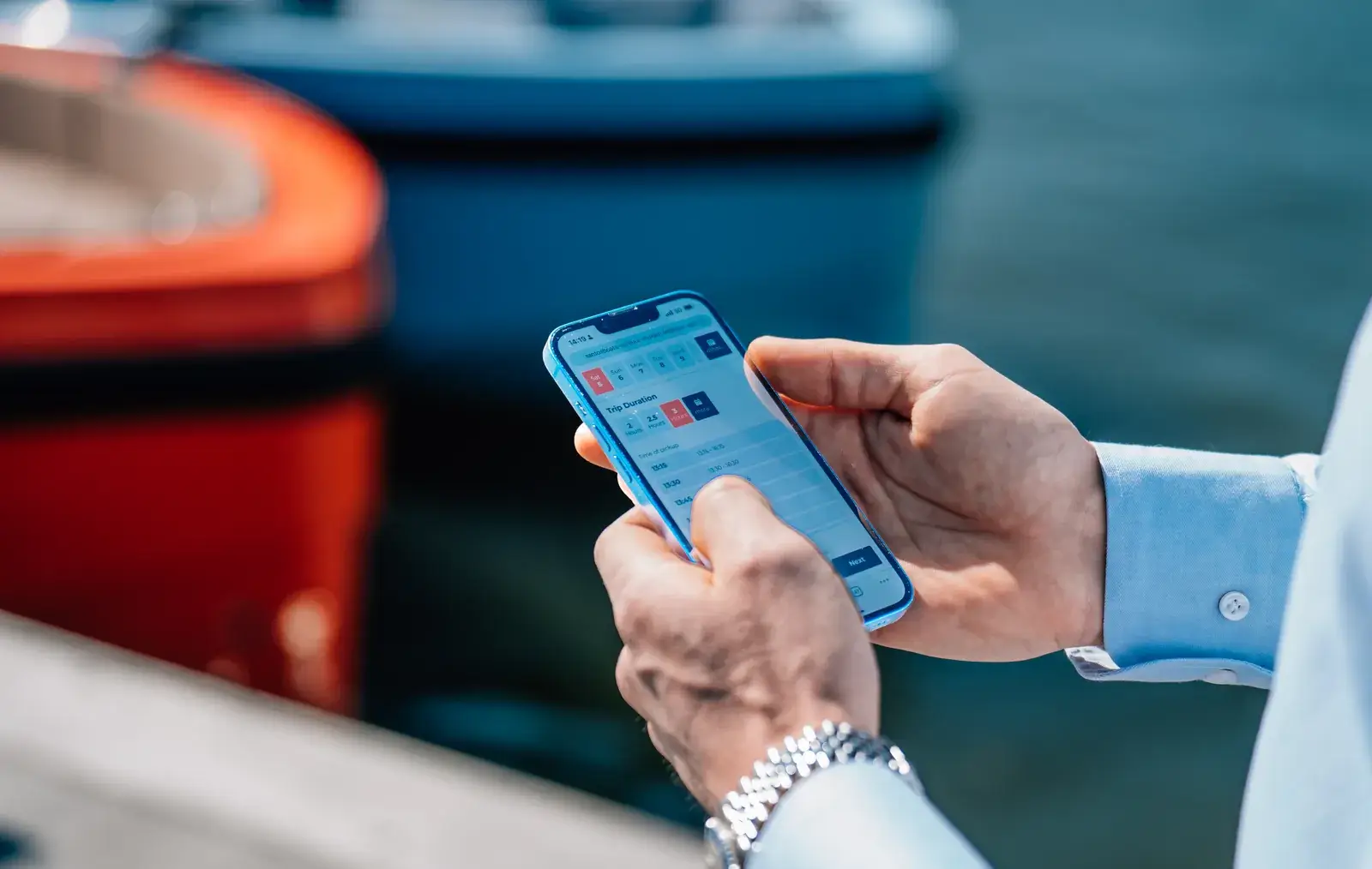 Een hand met een telefoon waarop een boeking openstaat, naast een boot aan de steiger