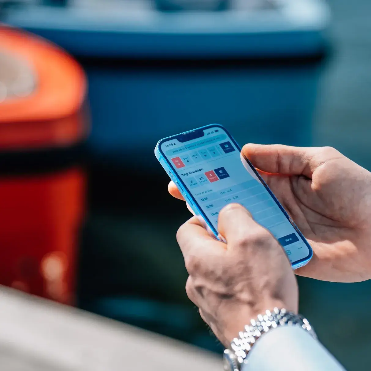 Eine Hand hält ein Handy mit einer offenen Bootsbuchung, dahinter orange Mietboote