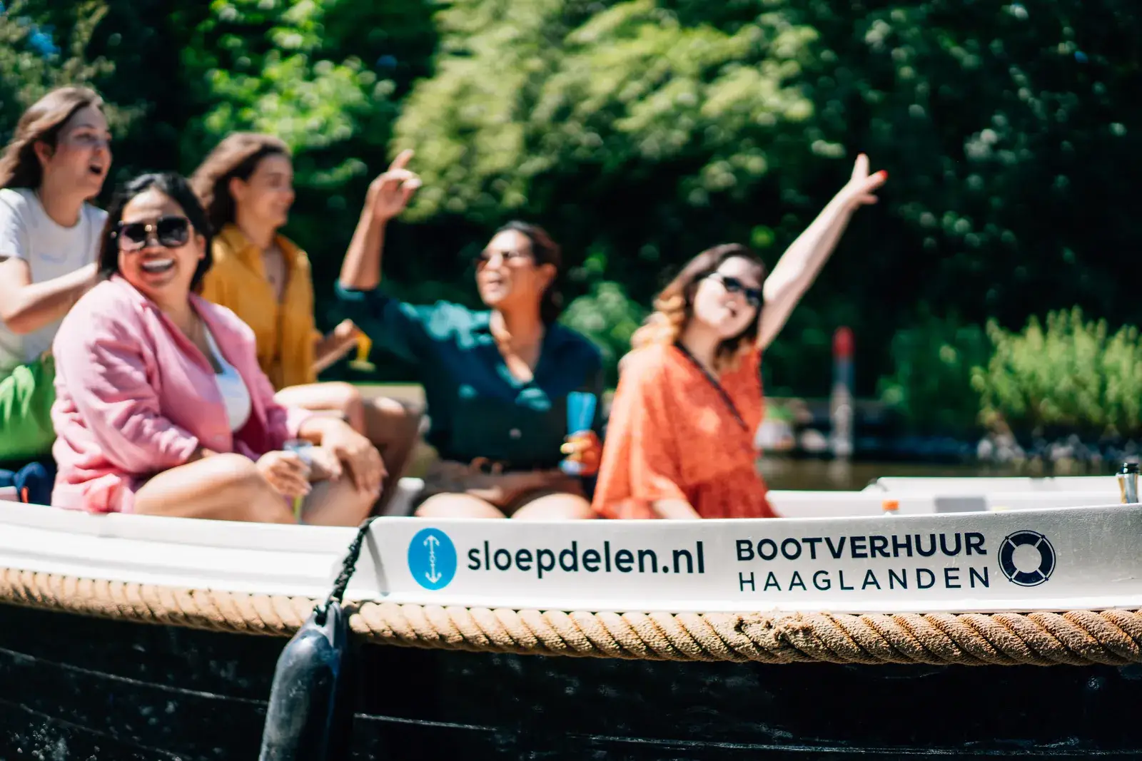 Vrienden die lachen op een sloep met de naam en de website van het verhuurbedrijf op de zijkant