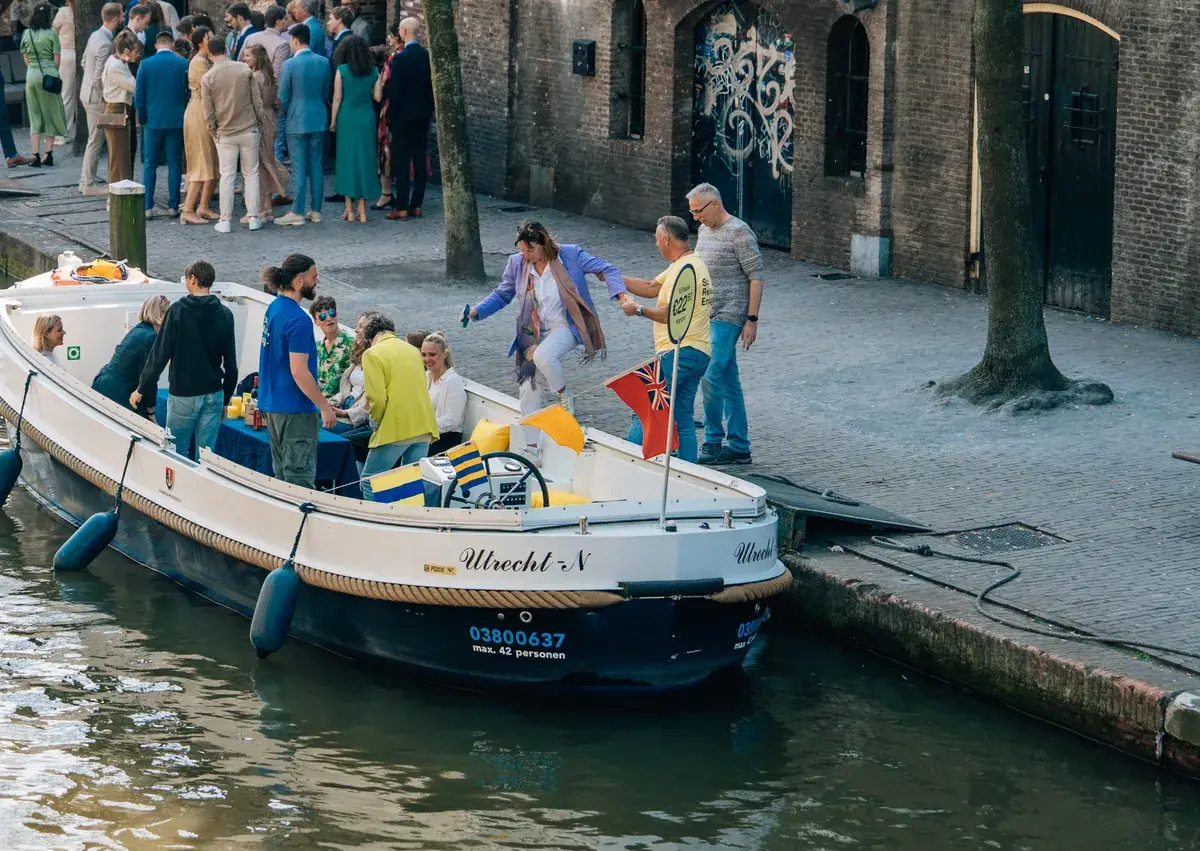 Un groupe monte à bord d'un bateau-promenade ouvert sur un quai de canal, le skipper les aide à embarquer