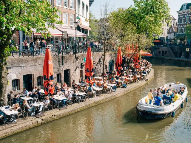 An open canal cruise boat on a canal in Utrecht, passing the terraces of the old wharf cellars