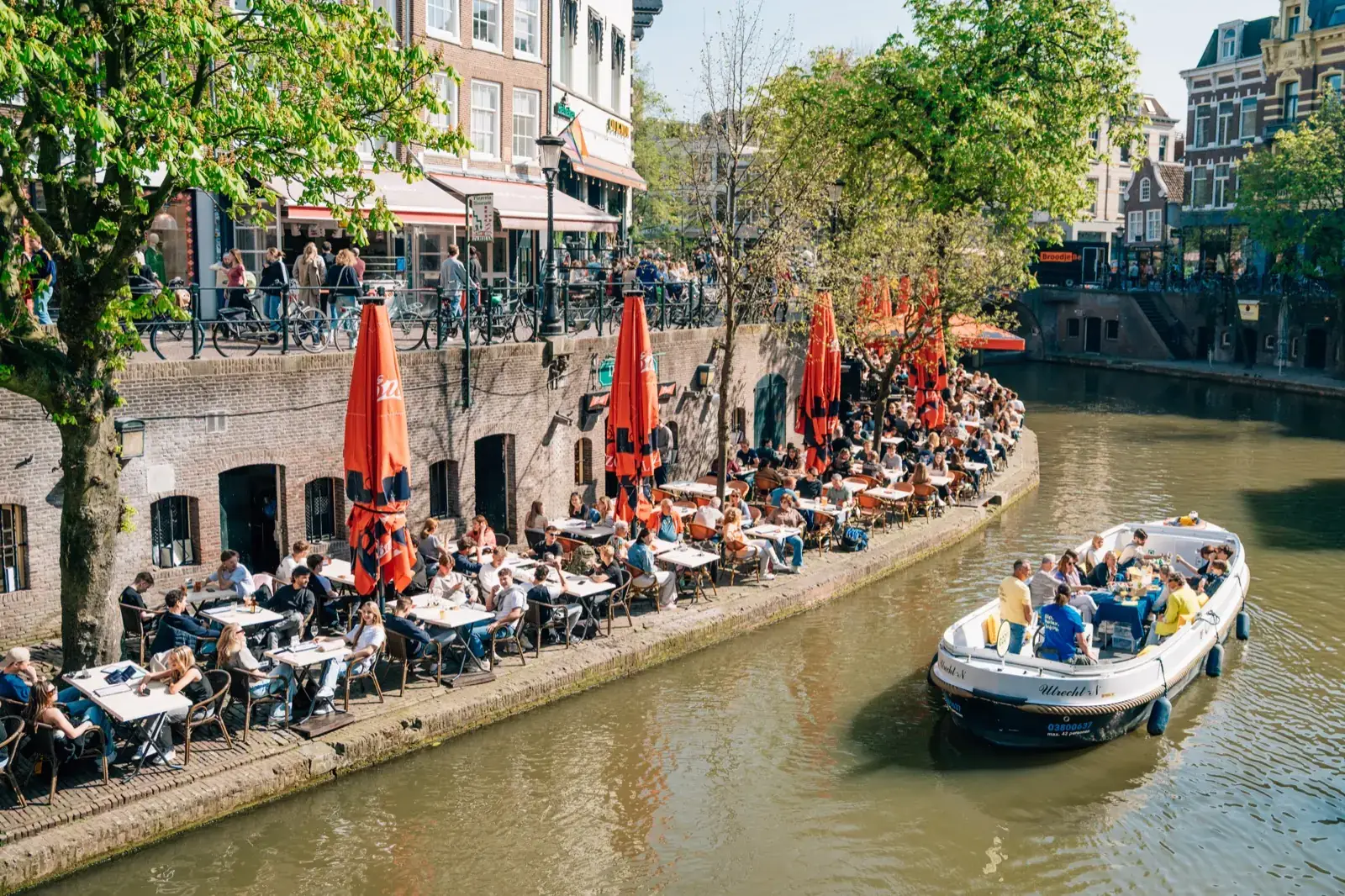 An open cruise boat on a canal in Utrecht, passing terraces built into the old wharf cellars