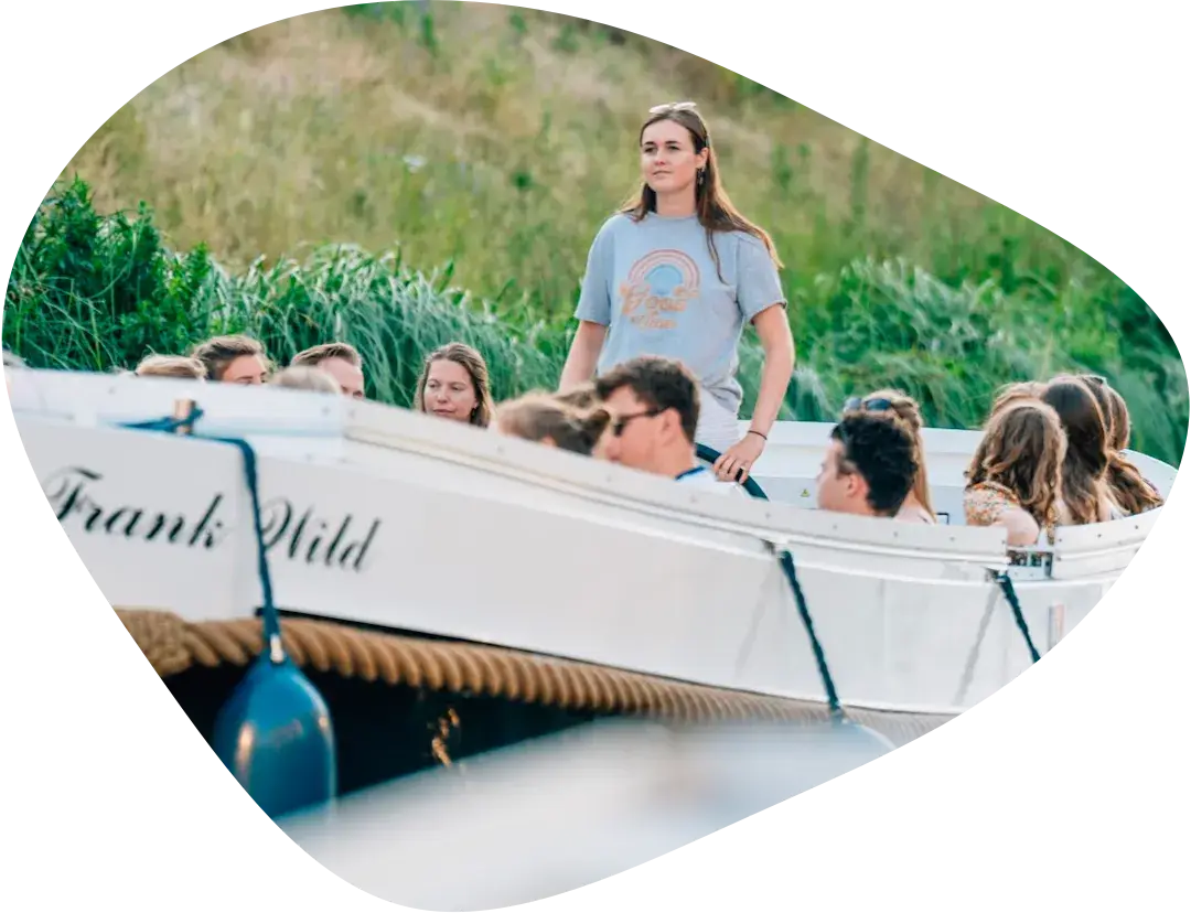 A skipper steering a full open tour boat along a canal