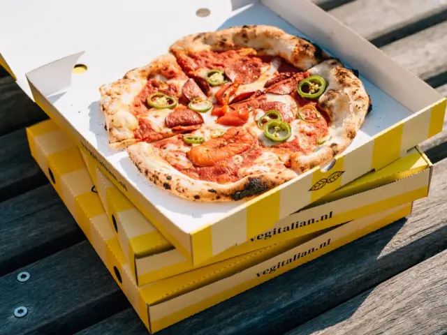Three pizza boxes stacked on the planks of a dock, the top one open