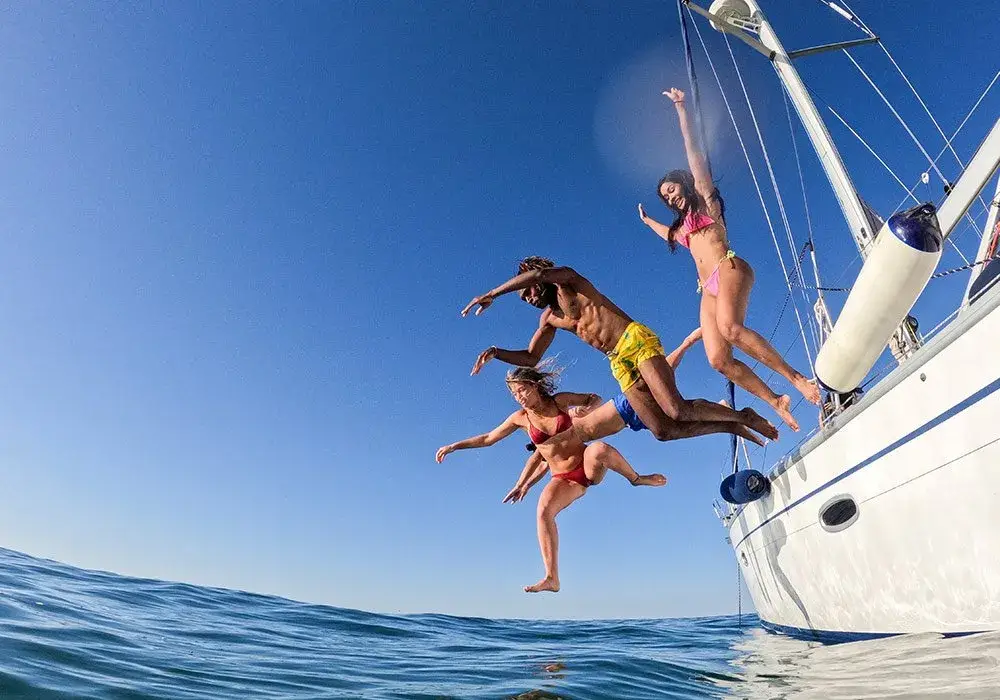 Four people jumping off a sailing yacht into the sea