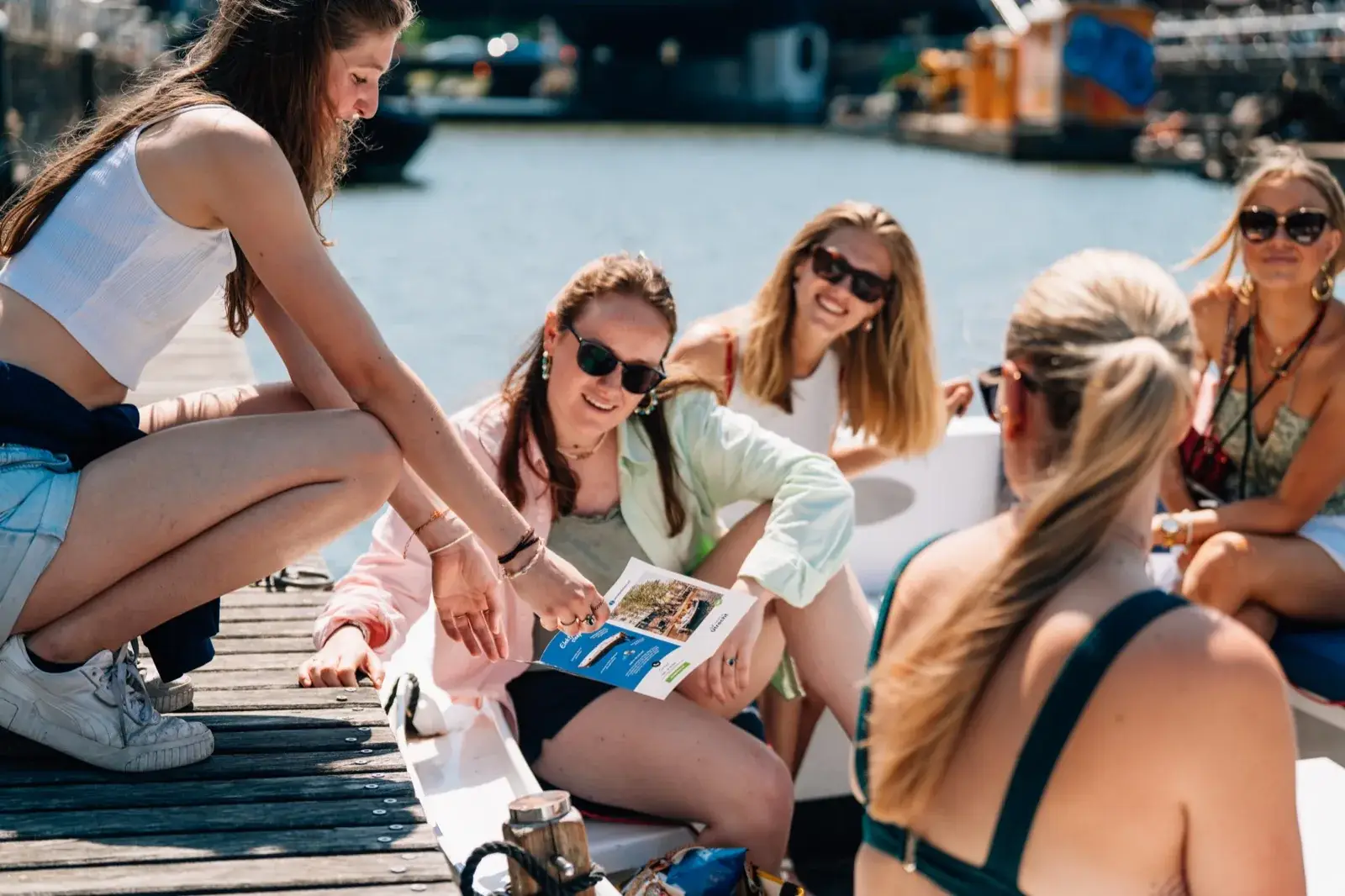 A crew member crouching on the dock shows a leaflet to a group seated in an open boat