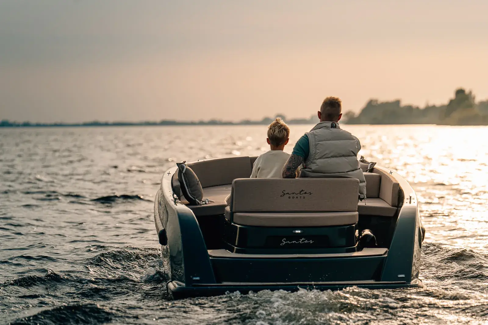 Two people in an electric boat heading out over a lake at sunset