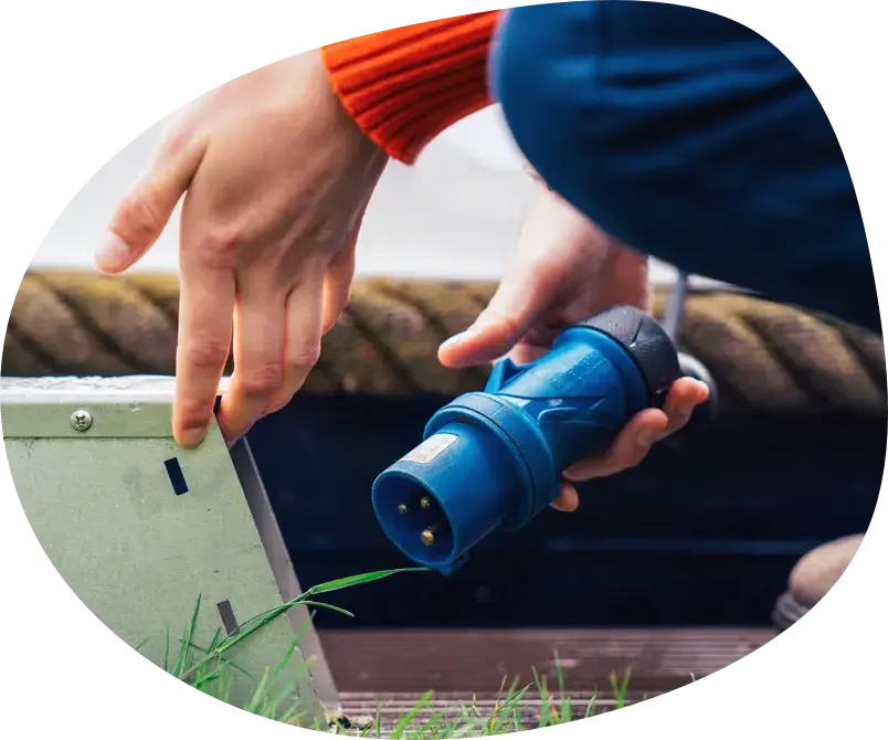 A hand plugs a blue charging cable into a power box on the dock