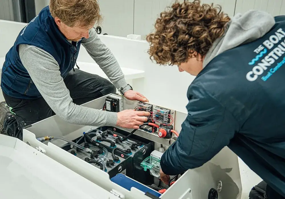 Two engineers in branded jackets fitting a battery pack into a boat