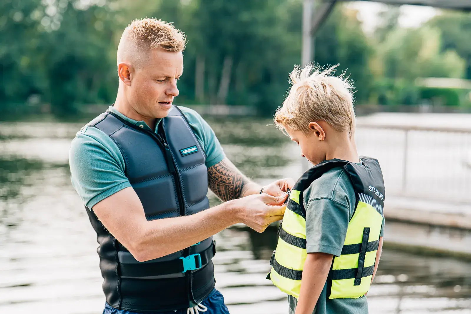 Een man die een geel zwemvest vastmaakt bij een jongen op de steiger