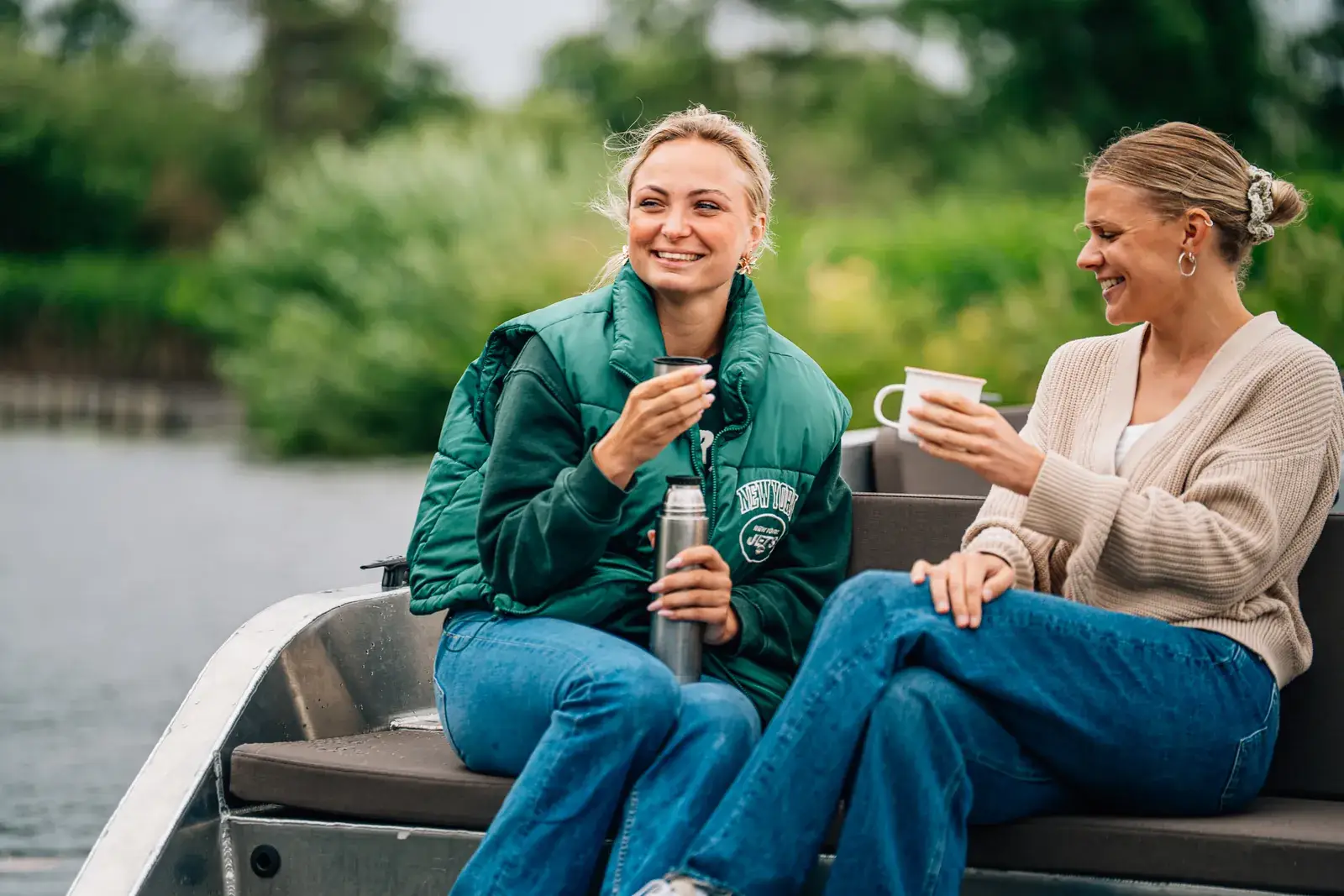 Twee vrouwen met een beker koffie lachen op de bank van een open elektrische boot op een rivier
