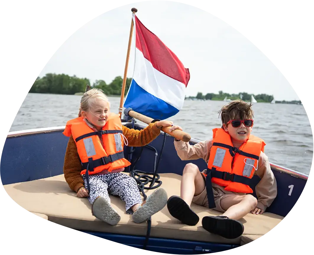 Two children in life jackets sitting in a boat under a Dutch flag