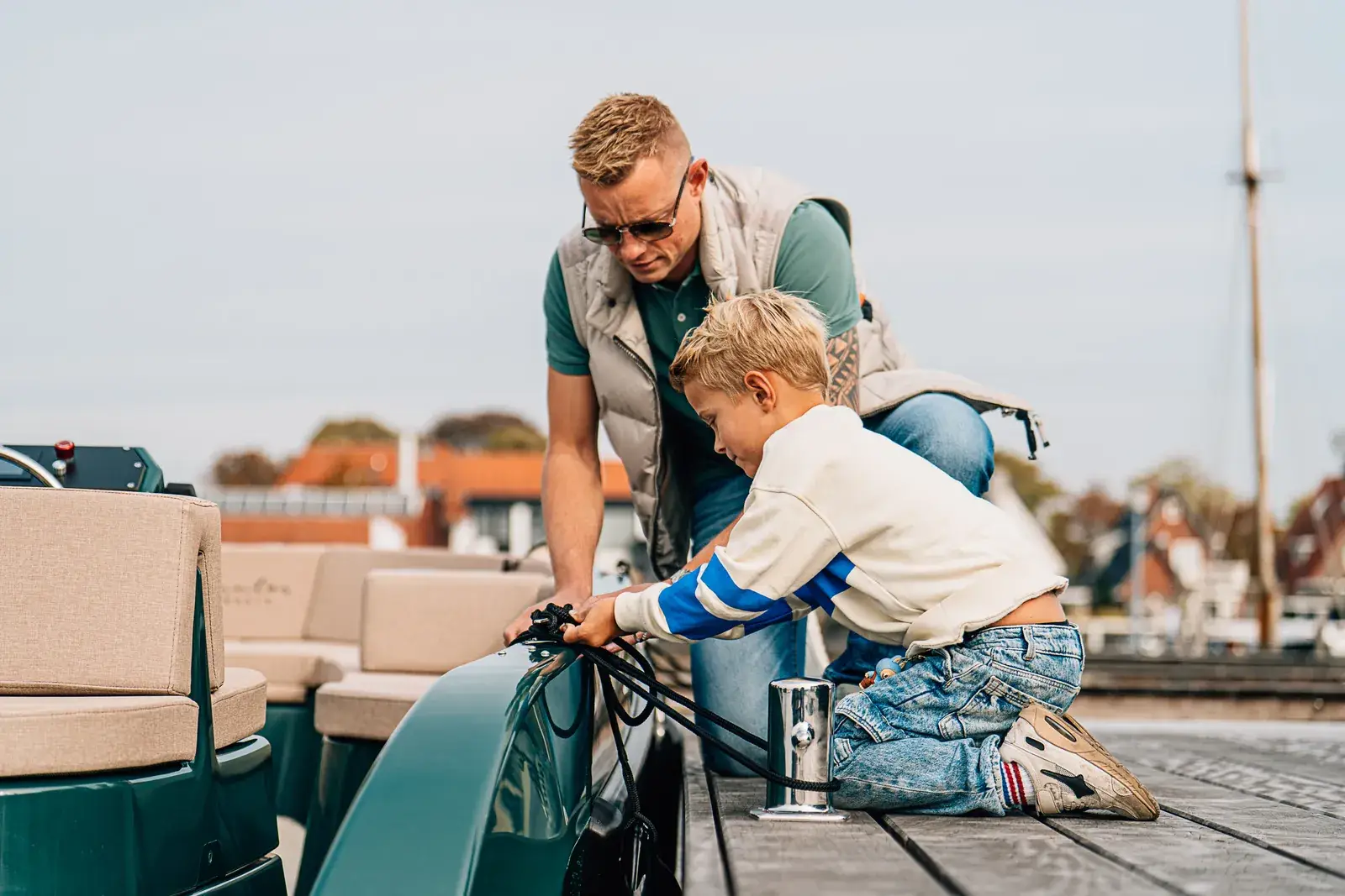 Een man en een jongen die een groene elektrische boot vastleggen aan een houten steiger