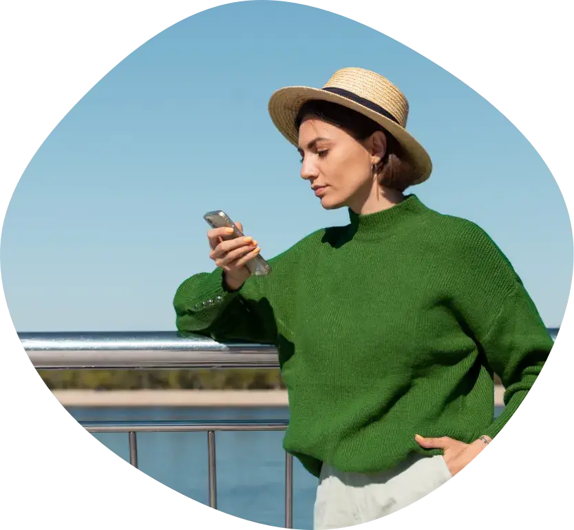 A woman in a straw hat looking at her phone by the water
