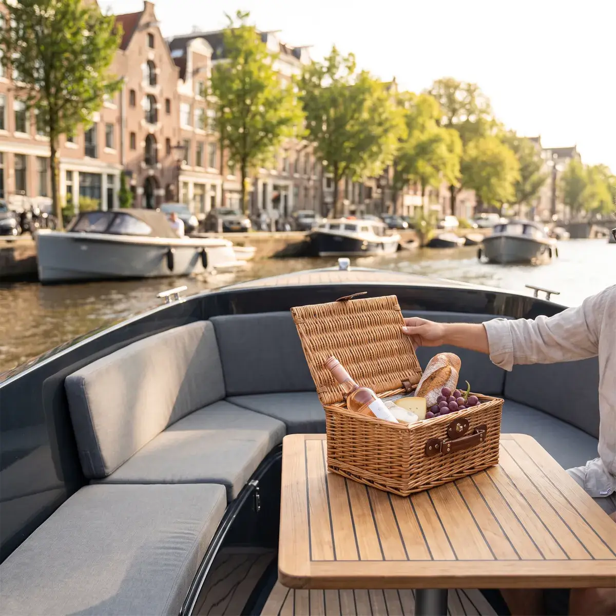 Una cesta de pícnic de mimbre con una barra de pan, queso, uvas y una botella sobre la mesa de un pequeño barco abierto en los canales de Ámsterdam
