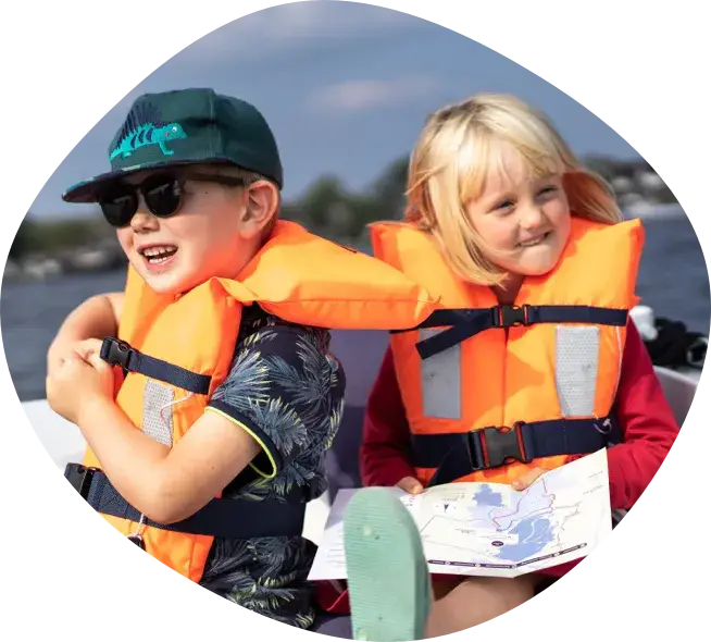 Two children in life jackets laughing on board, the boy in a cap and the girl holding a map