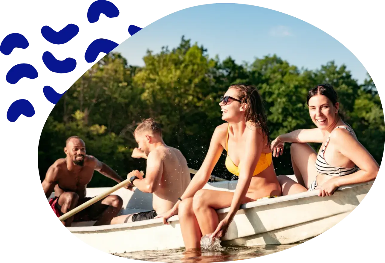 Vier Freunde in einem Ruderboot, einer rudert, am Ufer stehen Bäume