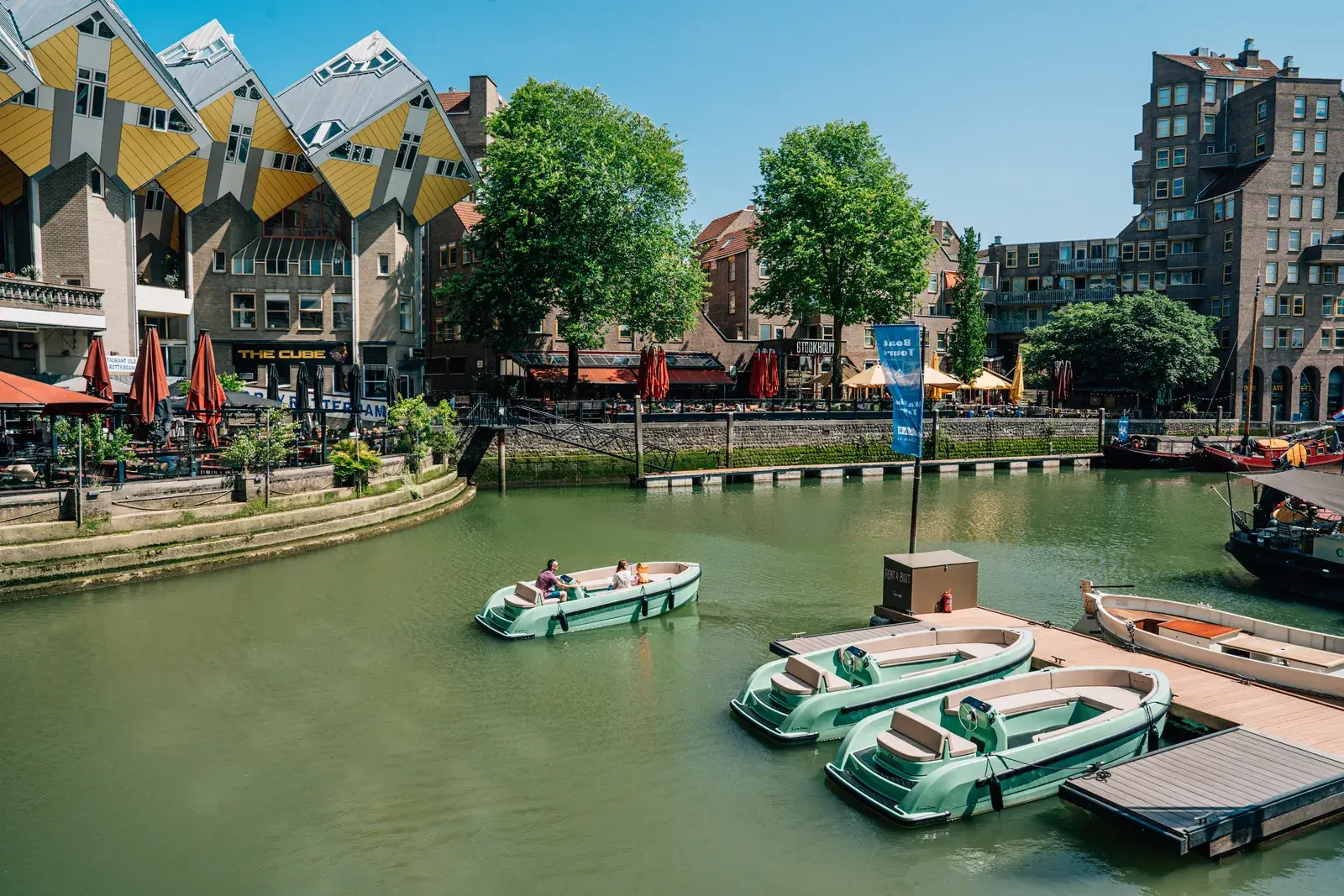 Groene huursloepen aan een drijvende steiger bij de kubuswoningen in Rotterdam, één vaart net weg