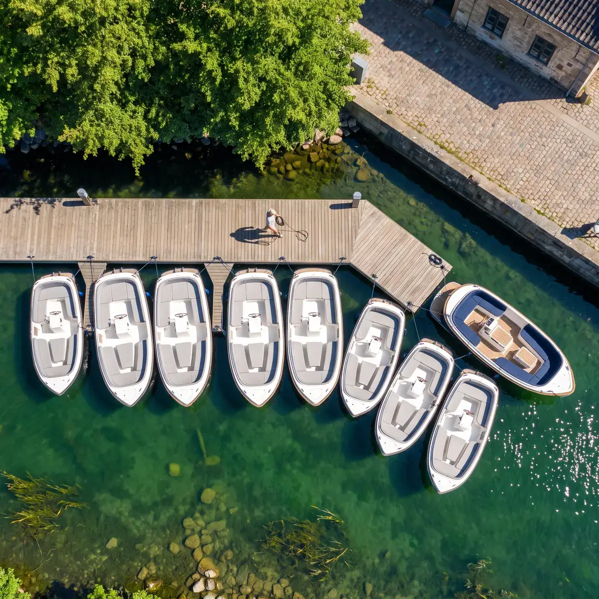 Identical electric boats moored side by side, with one larger boat of another model at the end of the row, seen from above