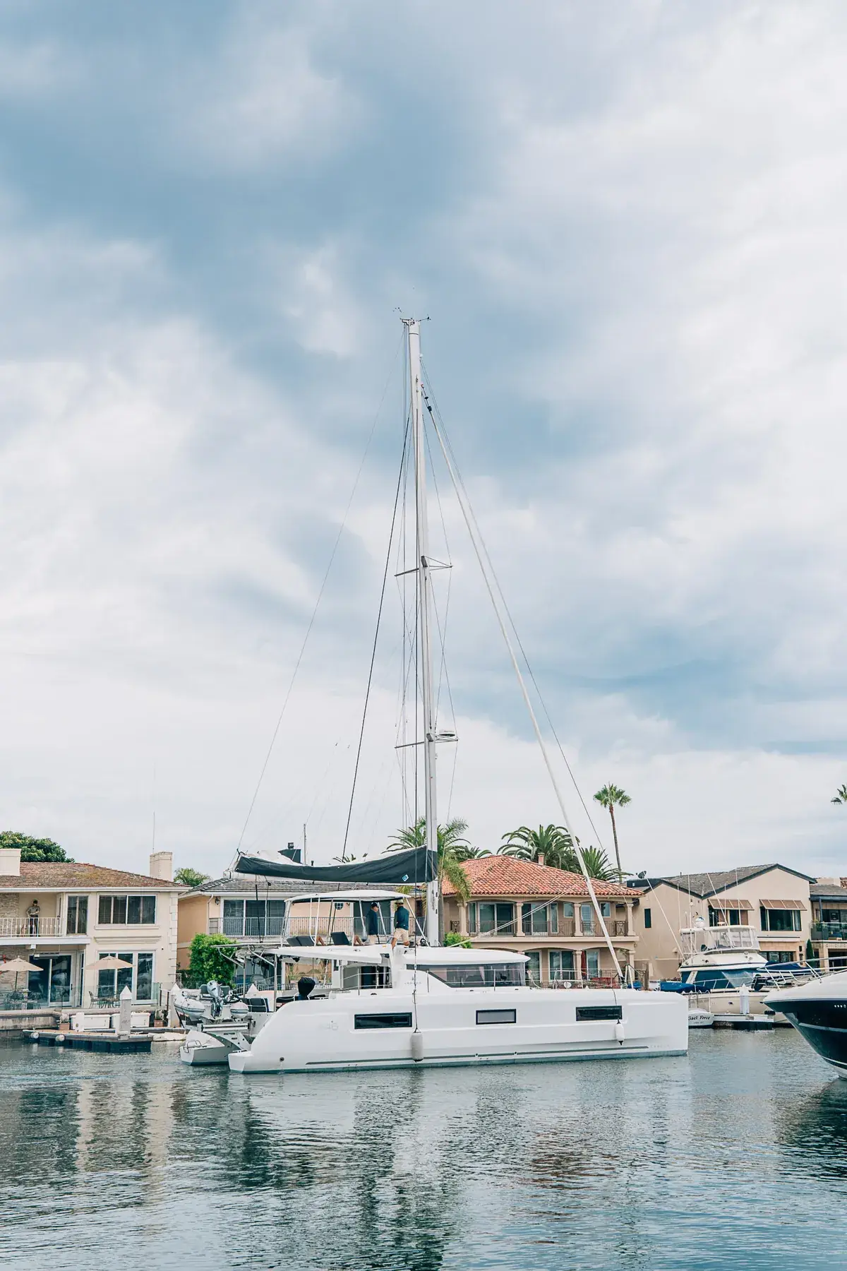 Ein Segelkatamaran an einem Kanal in Newport Beach, Kalifornien, mit Häusern und Palmen dahinter