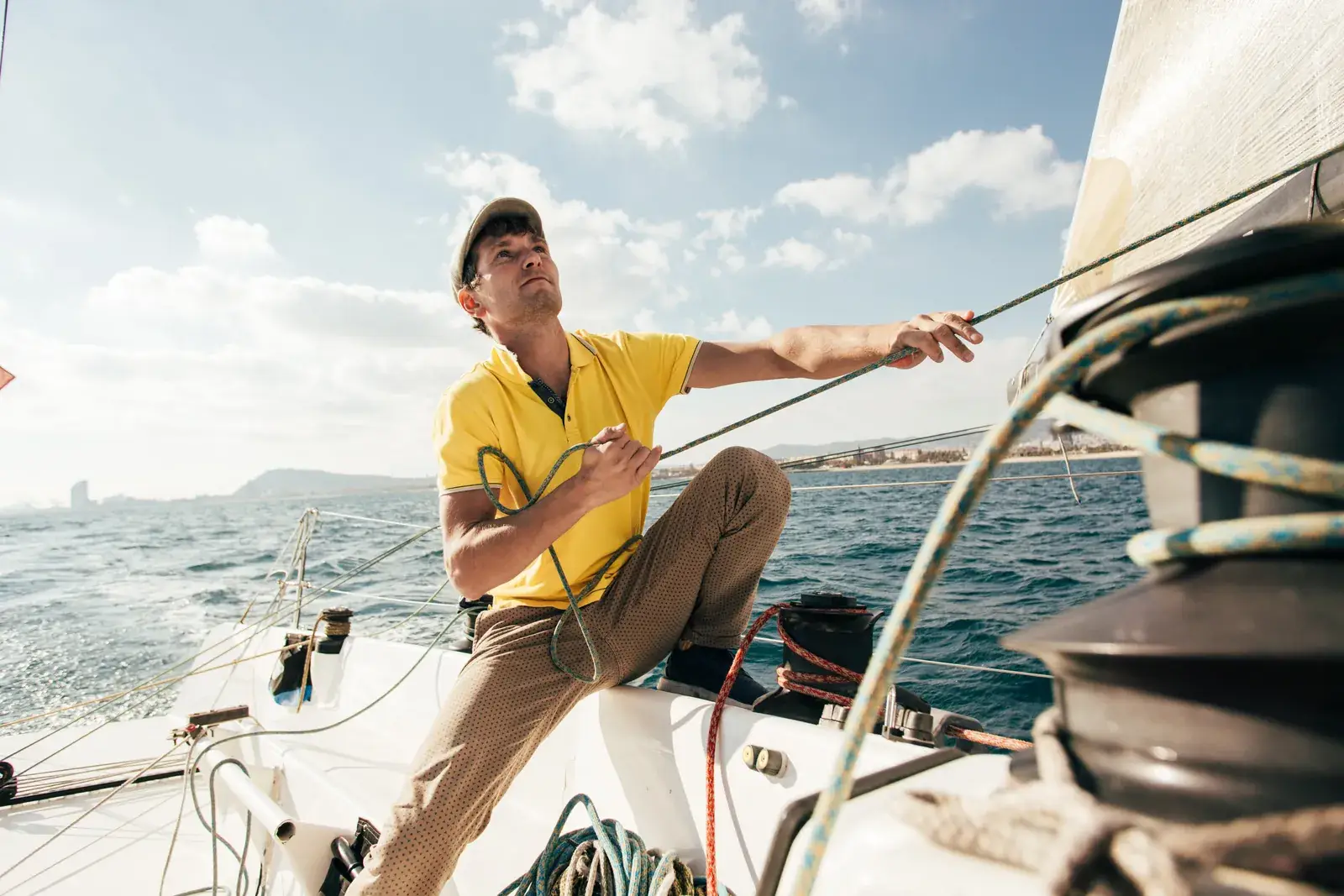 Ein Segler im gelben Poloshirt holt auf dem Deck eines Segelboots eine Schot dicht