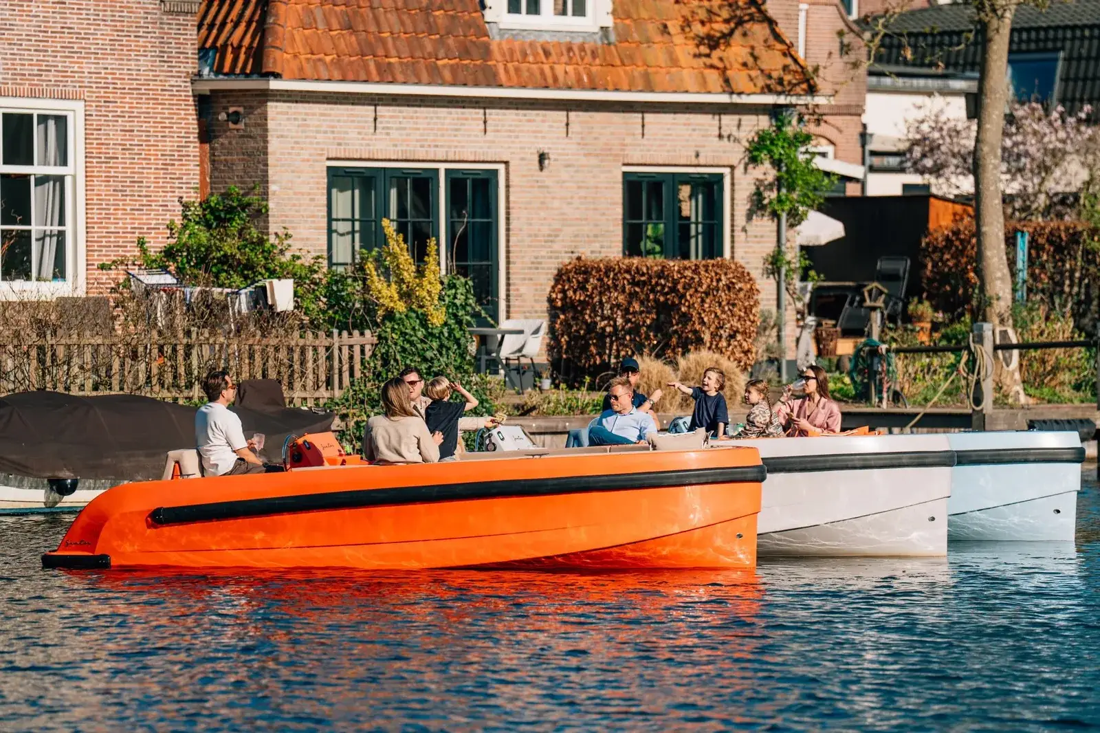 Ein orangefarbenes Elektroboot Santos One mit einer Familie an Bord, dahinter zwei weitere Boote von Santos