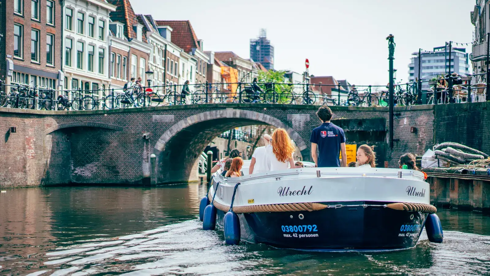 Een schipper die een sloep vol gasten onder een oude brug door stuurt op een Utrechtse gracht