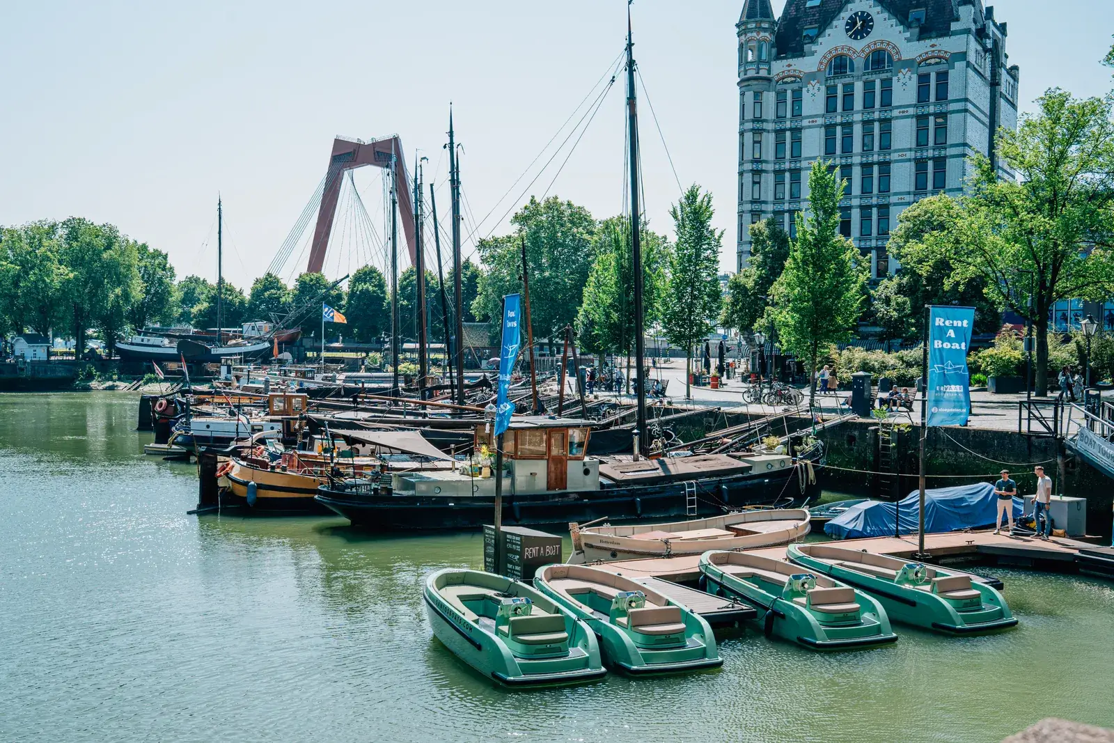 Green open rental motorboats at a small dock in the Oude Haven of Rotterdam, the Willemsbrug behind