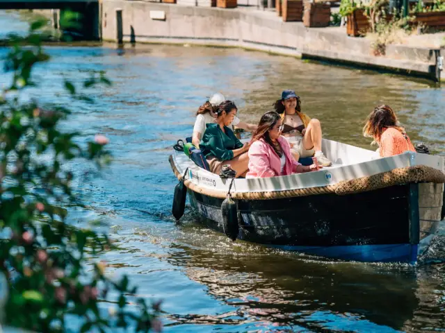 An open rental motorboat on a tree-lined canal in The Hague with friends aboard