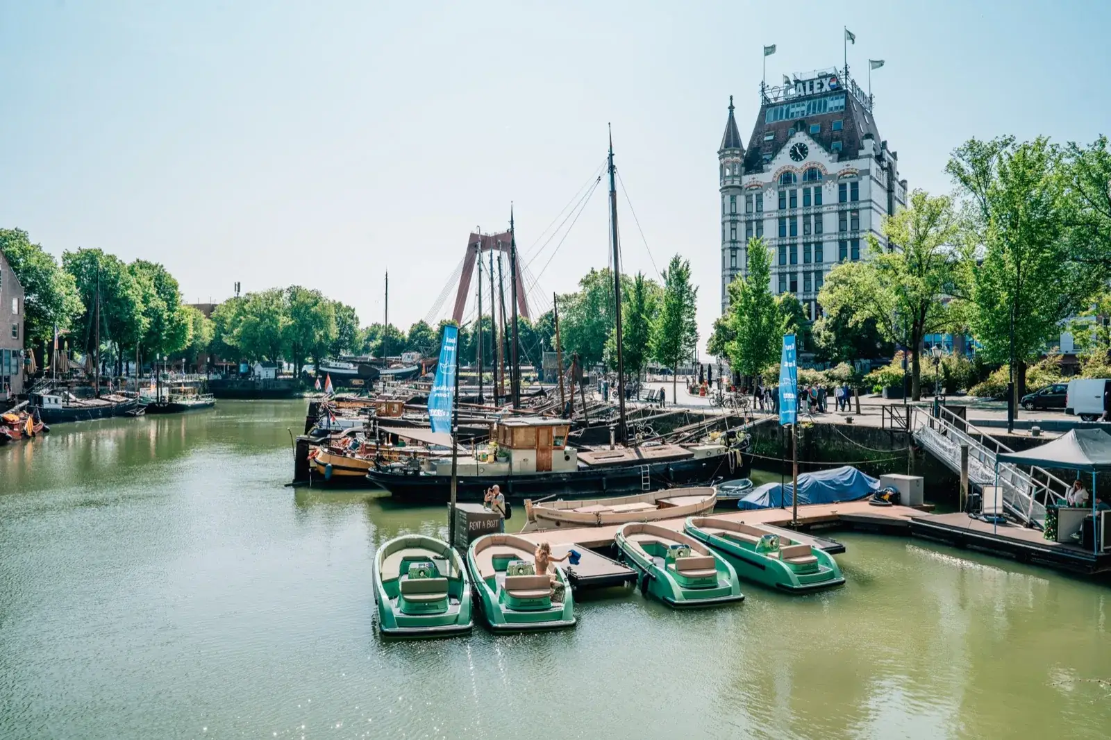 Four mint-green rental sloops moored in a row at a floating dock in the old harbor of Rotterdam, historic barges and the Witte Huis behind them