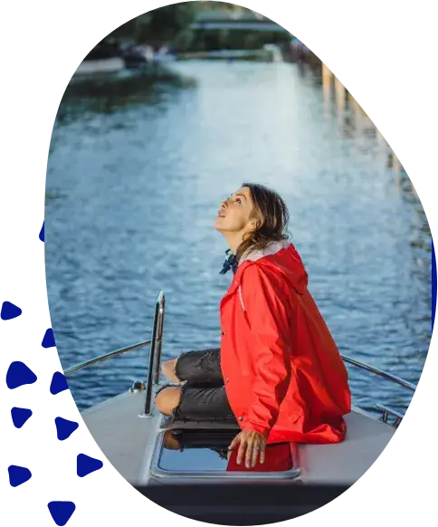 A woman in a red jacket sitting at the bow of a boat, looking out over the water