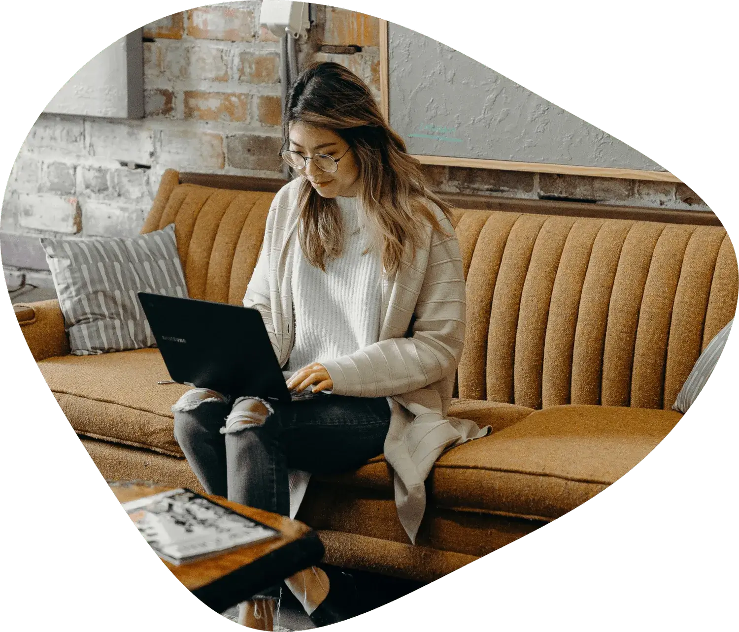 Eine Frau arbeitet drinnen auf einem Sofa an einem Laptop