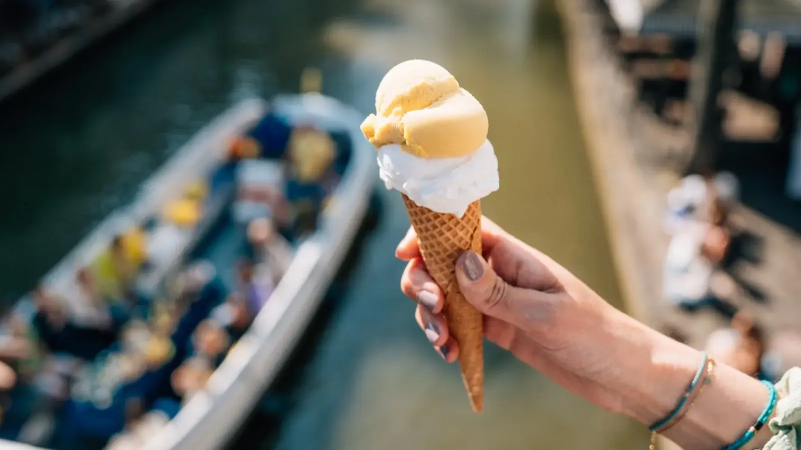 An ice cream held up in front of an open tour boat full of people