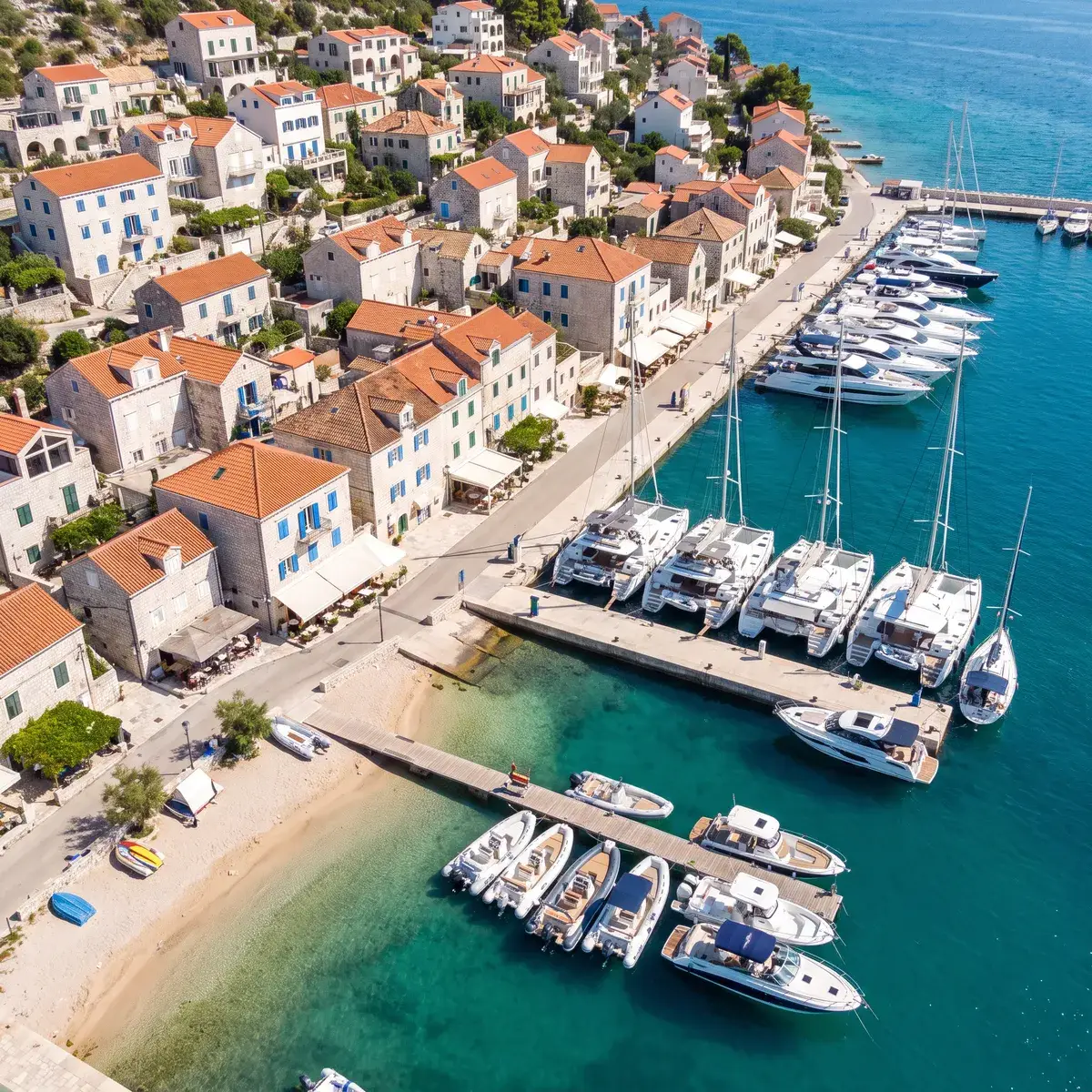 A Mediterranean coastal town from above, with a marina and a beach jetty full of boats