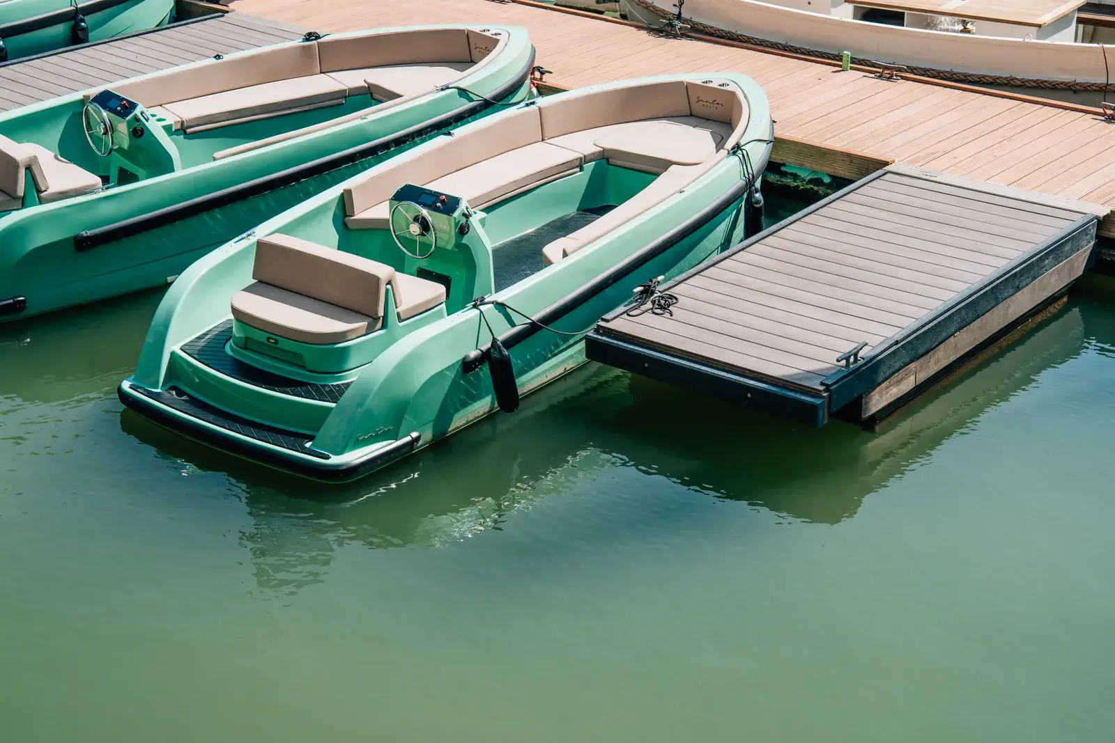 Two green open rental motorboats moored side by side at a floating dock