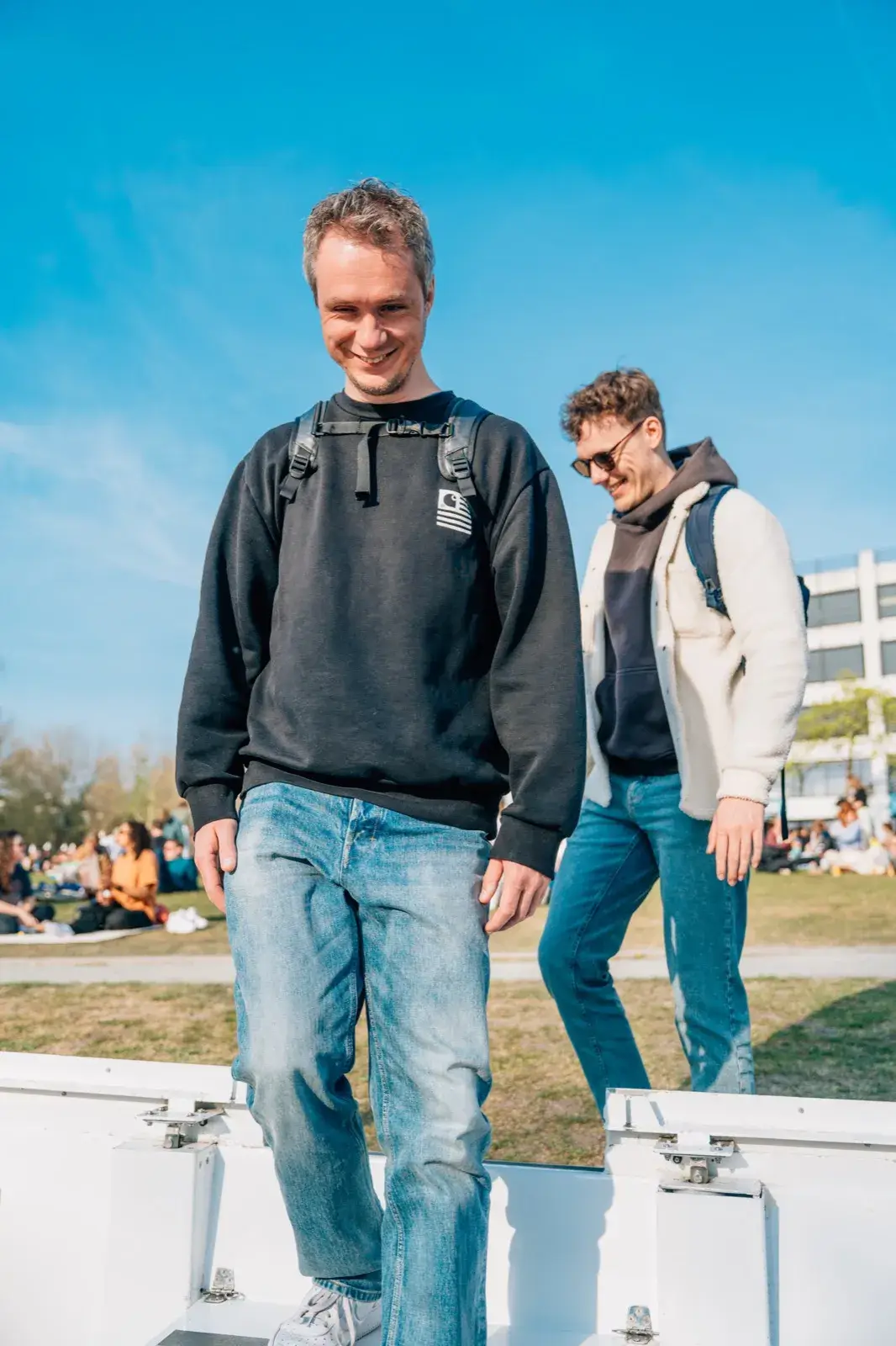 Two men in jeans step laughing into a white boat on a sunny spring day in Utrecht