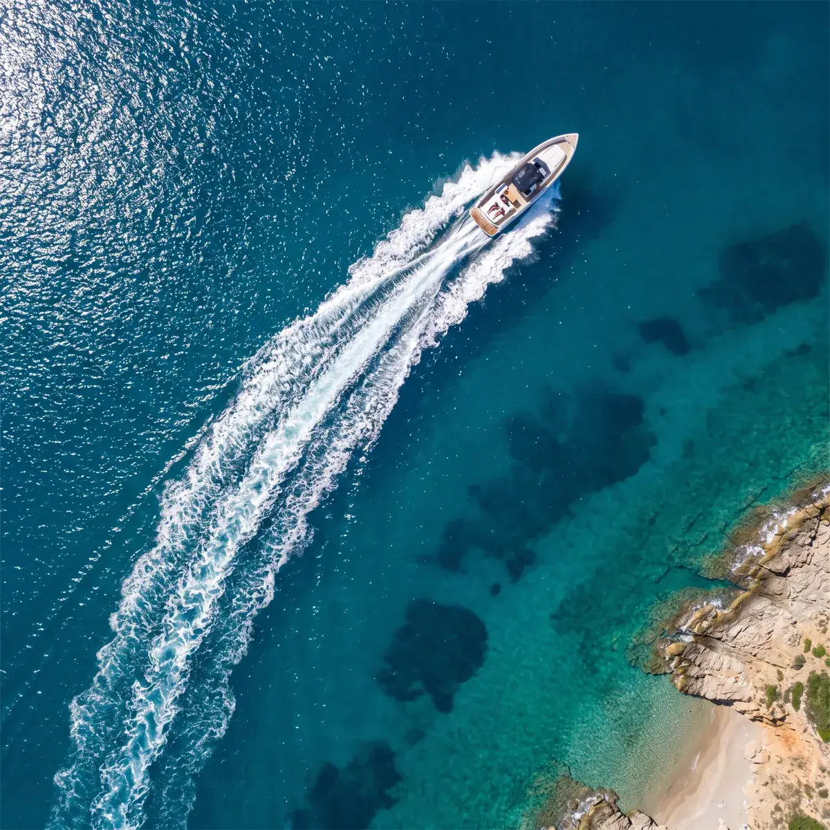One open boat crossing a turquoise bay, its white wake drawing a long line behind it, seen from above